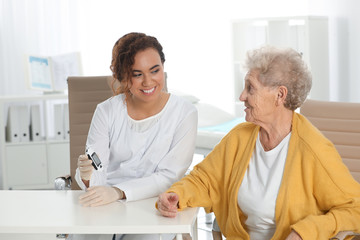Obraz premium Doctor checking patient's blood sugar level with digital glucometer at table. Diabetes control