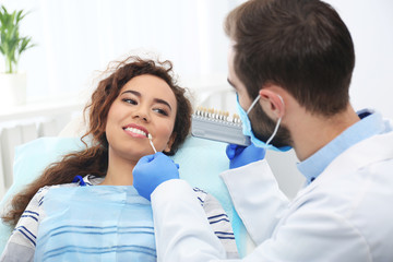 Dentist matching patient's teeth color with palette in office