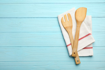 Wooden spatula, fork and napkin on color background, top view with space for text