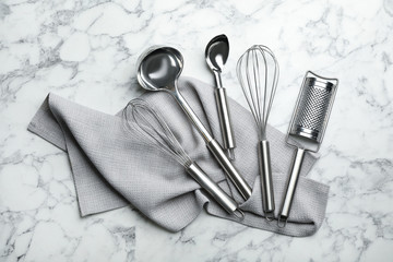 Set of clean kitchen utensils and napkin on marble background, top view