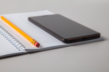 An open notebook with a pencil lying on it and a mobile phone