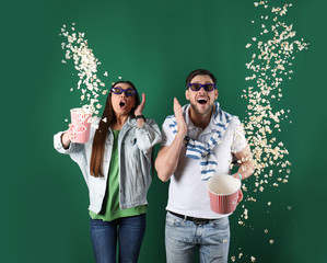 Emotional couple with 3D glasses throwing popcorn on color background