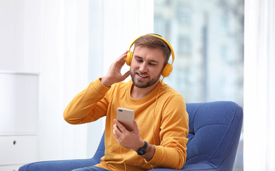 Young man with headphones and mobile device sitting in armchair at home