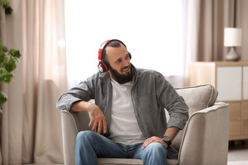 Mature man with headphones resting in armchair at home