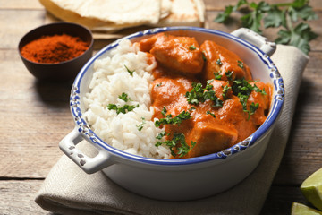 Delicious butter chicken with rice in bowl served on wooden table