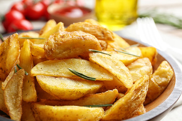 Plate with tasty baked potato wedges on table, closeup