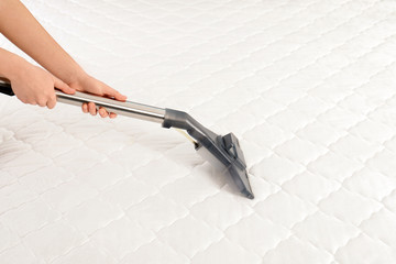 Woman disinfecting mattress with vacuum cleaner, closeup. Space for text