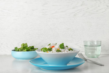 Plate of boiled rice with vegetables on table against light background. Space for text