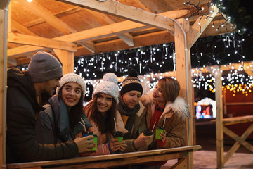 Happy friends with cups of mulled wine at winter fair