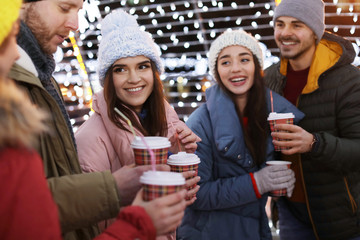 Happy friends with cups of mulled wine at winter fair