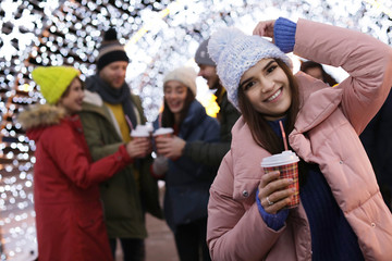 Happy woman with cup of mulled wine and friends at winter fair. Space for text