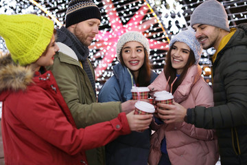 Happy friends with cups of mulled wine at winter fair