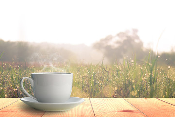 Hot coffee on Wooden table and grass field at morning