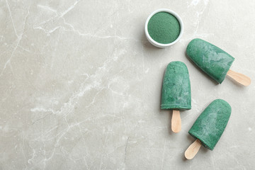 Flat lay composition with delicious spirulina popsicles and powder on grey background. Space for text