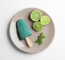 Plate with delicious spirulina popsicle and lime on white background, top view