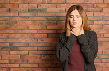 Woman suffering from cough near brick wall. Space for text
