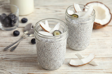 Tasty chia seed pudding with coconut in jars and ingredients on table