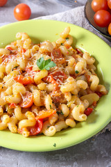 Green plate full of with fresh homemade elbow macaroni pasta , pieces of bell pepper, cherry tomato halves, grated cheese and parsley. Tasty meal