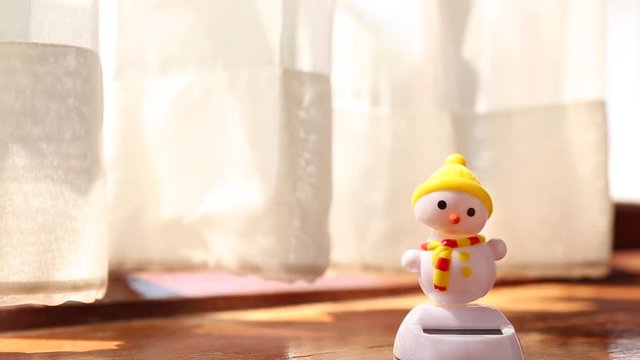 snowman doll dancing besides window with transparent curtain 