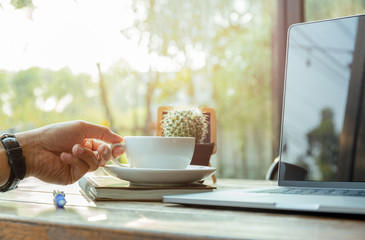 Businessman hand holding coffee cup with laptop on the table.