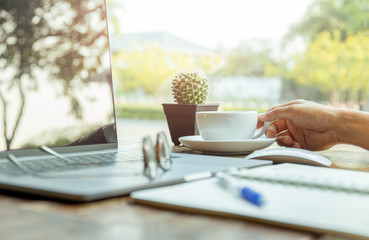 Businessman holding cup of coffee with laptop on the table in cafe.