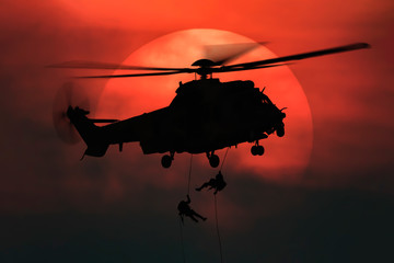 Shot of rescue helicopter hopping in front of the big sun with two soldiers rappelling from high