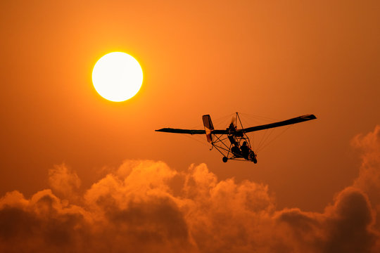 A microlight aircraft with two passengers with the sun and cloud