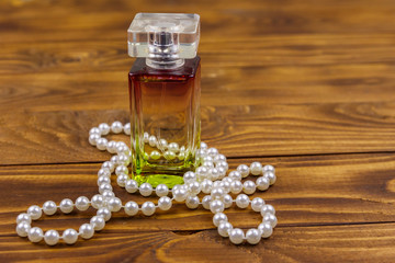 Obraz na płótnie Canvas Bottle of perfume and pearl necklace on wooden background