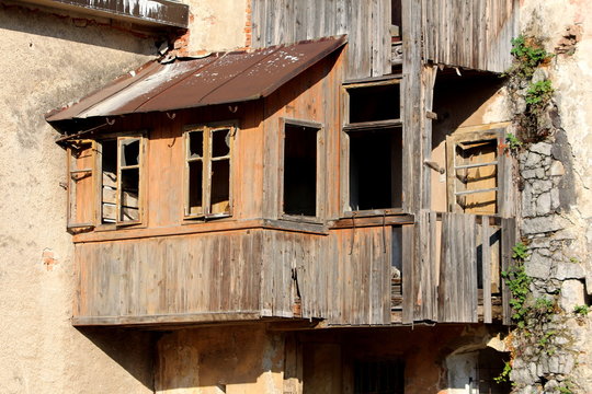 Ruins of wooden house addon with destroyed boards and missing glass on windows and with rusted roof waiting to be demolished and rebuilt on warm sunny day