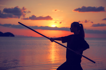 Young beautiful girl woman blond doing kung fu with bamboo stick on the seashore at sunset