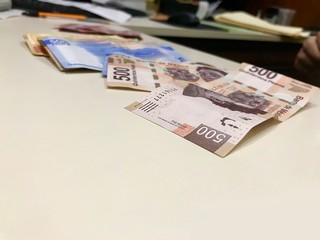Many mixed Mexican peso bills spread over a beige desk
