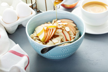 Healthy oatmeal with sliced apple and almonds for breakfast with maple syrup poured over