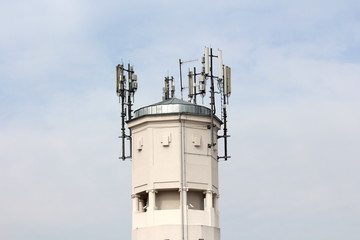 Top of large concrete industrial complex tower with multiple cell phone antennas and transmitters surrounded with security cameras on cloudy blue sky background