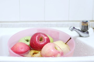 fresh apples in a pink bowl for preparing to wash in the white sink