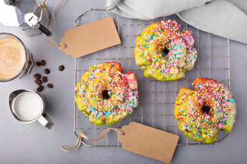 Colorful and festive unicorn donut with sprinkles on a baking rack with coffee and bakery tags, unicorn food trend