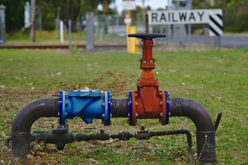 Red gas pipe with valve on green grass near railway
