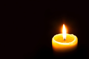 Single Burning Yellow Candle Glowing on a Dark Background. Copy Space.