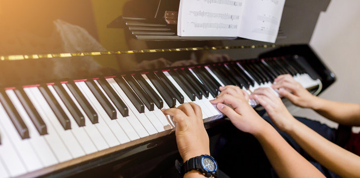 Selective focus to picture of young woman teaching a boy to play the piano with music notation
