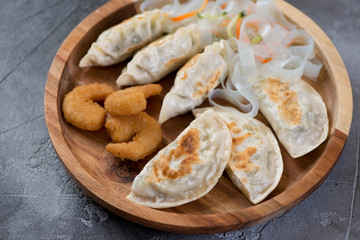 Close-up of different fried potstickers and panko breaded shrimps on a wooden serving tray, selective focus, studio shot
