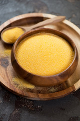 Wooden bowl with raw polenta on a wooden serving tray, vertical shot, close-up