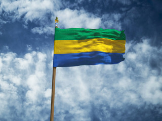 Gabon flag Silk waving flag of Gabon made transparent fabric with wooden flagpole gold spear on background sunny blue sky white smoke clouds real retro photo Countries of world 3d illustration
