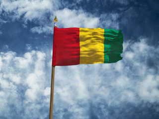 Guinea flag Silk waving flag of Guinea made transparent fabric with wooden flagpole gold spear on background sunny blue sky white smoke clouds real retro photo Countries of world 3d illustration