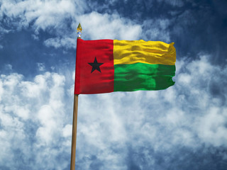 Guinea Bissau flag Silk waving flag of Guinea-Bissau made transparent fabric with wooden flagpole gold spear on background blue sky white smoke clouds real retro photo Countries world 3d illustration