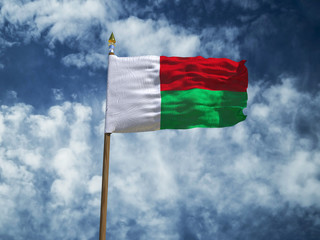 Madagascar flag Silk waving flag of Madagascar made transparent fabric with wooden flagpole gold spear on background blue sky white smoke clouds real retro photo Countries of world 3d illustration