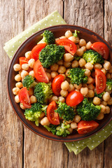 Vegetable salad from broccoli, chickpeas and fresh tomatoes with olive oil close-up. Vertical top view
