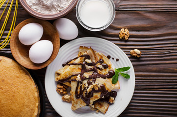 Flat lay French crepes with chocolate sauce walnuts eggs and flour on wooden kitchen table