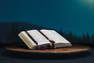Bible and the crucifix beads on a old round table. Beautiful stars night background. Religion concept.