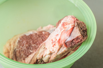 Raw veal meat is defrosted in green cooking plate.