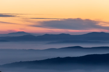 Plakat Beautifully colored sky at dusk, with mountains layers and mist between them