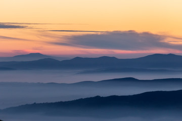 Beautifully colored sky at dusk, with mountains layers and mist between them